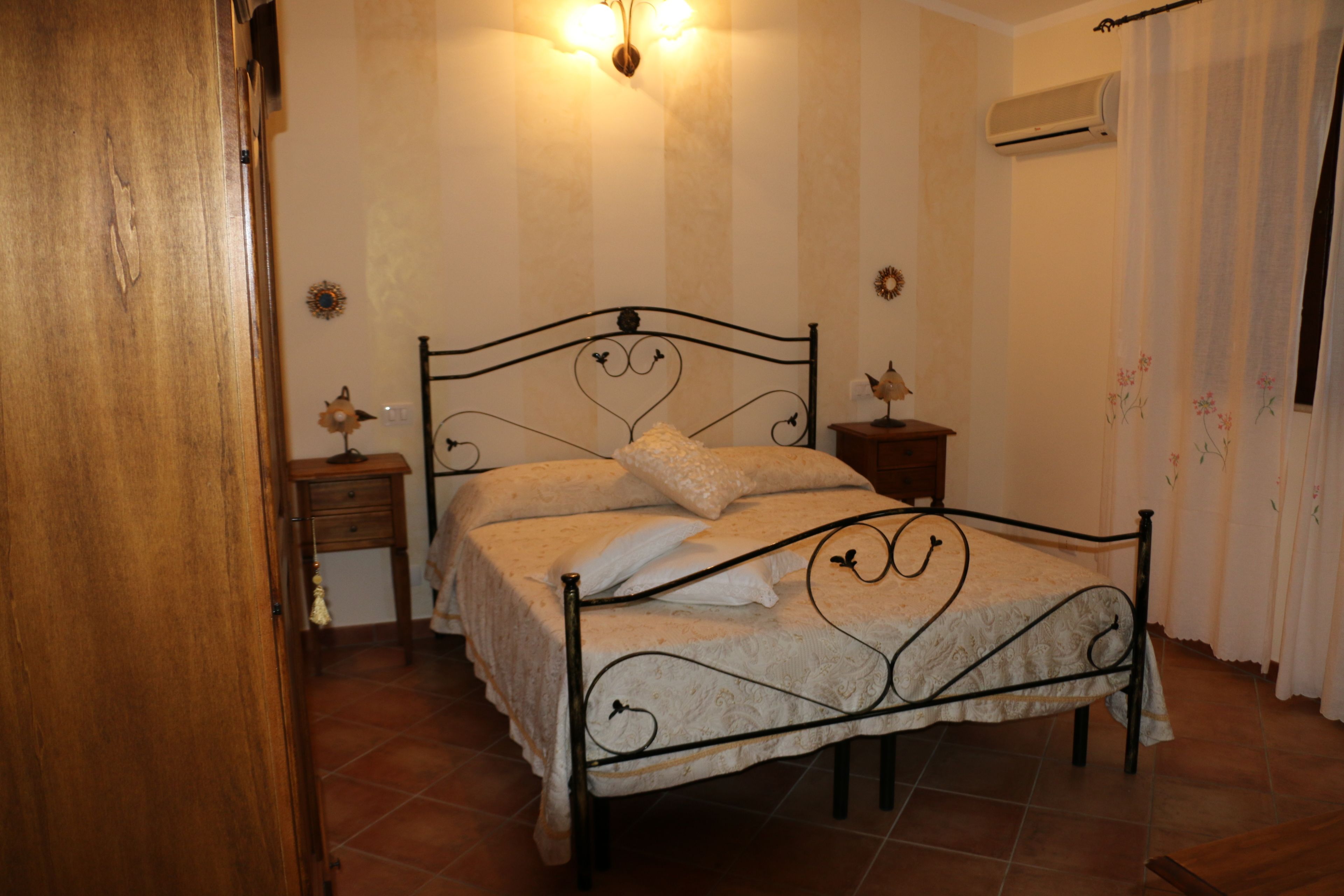 A bedroom with a metal bed frame, a bedside table with a lamp, and a wall-mounted air conditioner.
