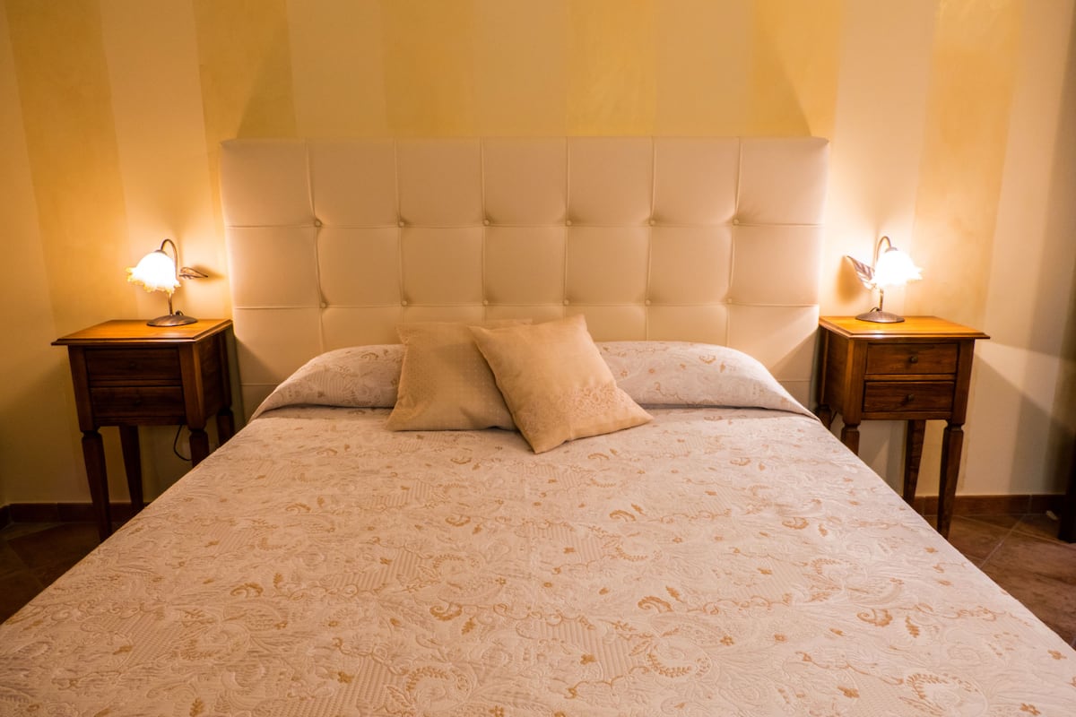 A large bed with a tufted headboard, two bedside tables with lamps, and two pillows.