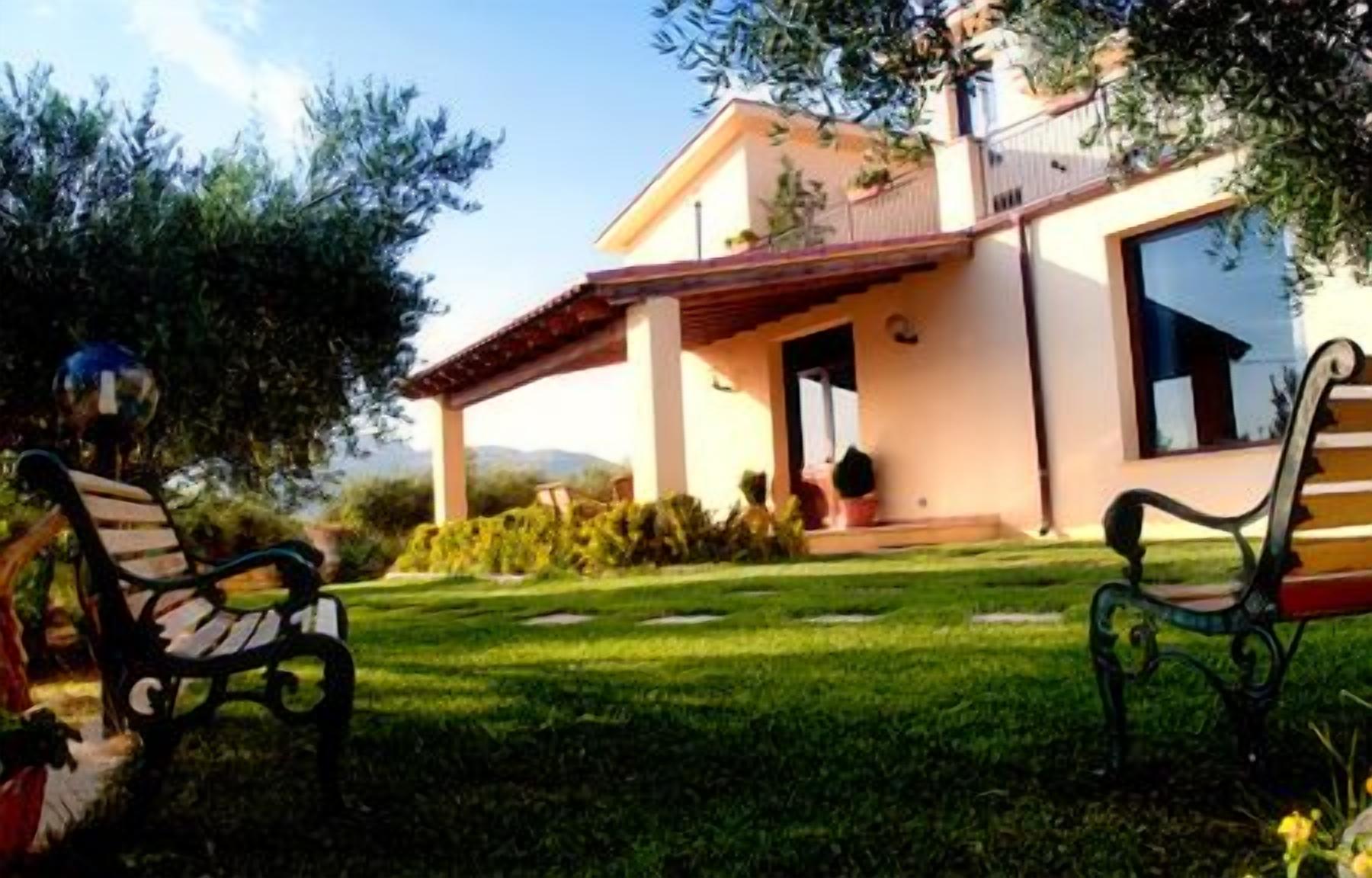 A house with a covered patio, a lawn, and two benches.