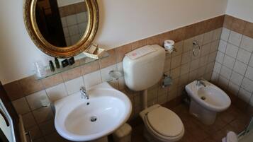 A bathroom with a white sink, toilet, bidet, and a large mirror with a gold frame.
