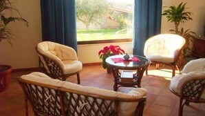 A room with wicker furniture, a glass table, and a view of a garden through a window. - Le Foglie d'Argento (Caltabellotta)
