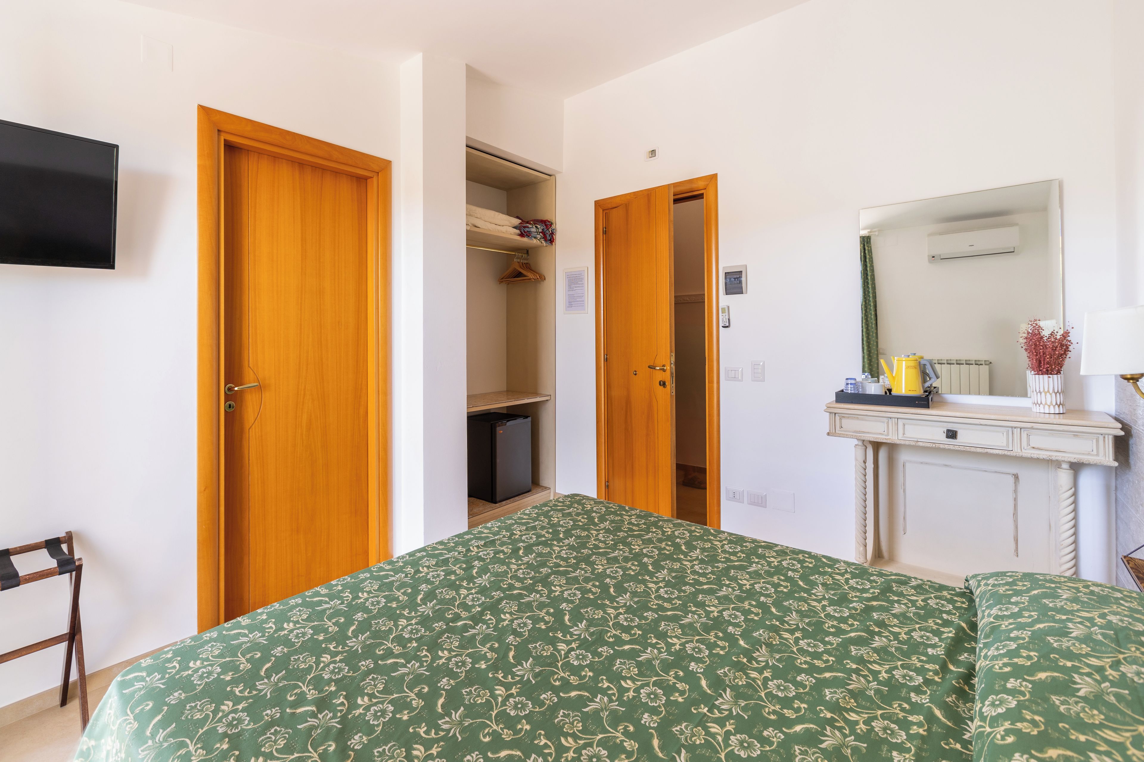 Une chambre d’hôtel avec un lit, un bureau, un miroir et une armoire.