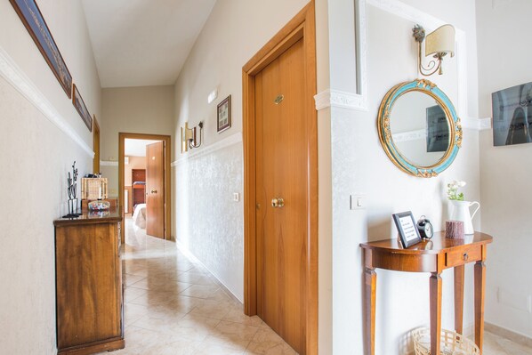 A hallway with a wooden door, a wall-mounted mirror, and a small table with a clock and picture frame. - Villa Vesta (Vieste)