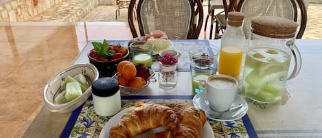 Una mesa de desayuno con cruasanes, fruta, café y jugo.