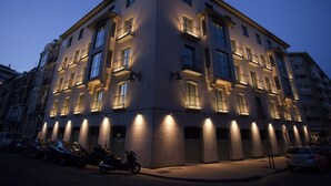 Un immeuble à plusieurs étages, doté de balcons et de fenêtres illuminées au crépuscule.