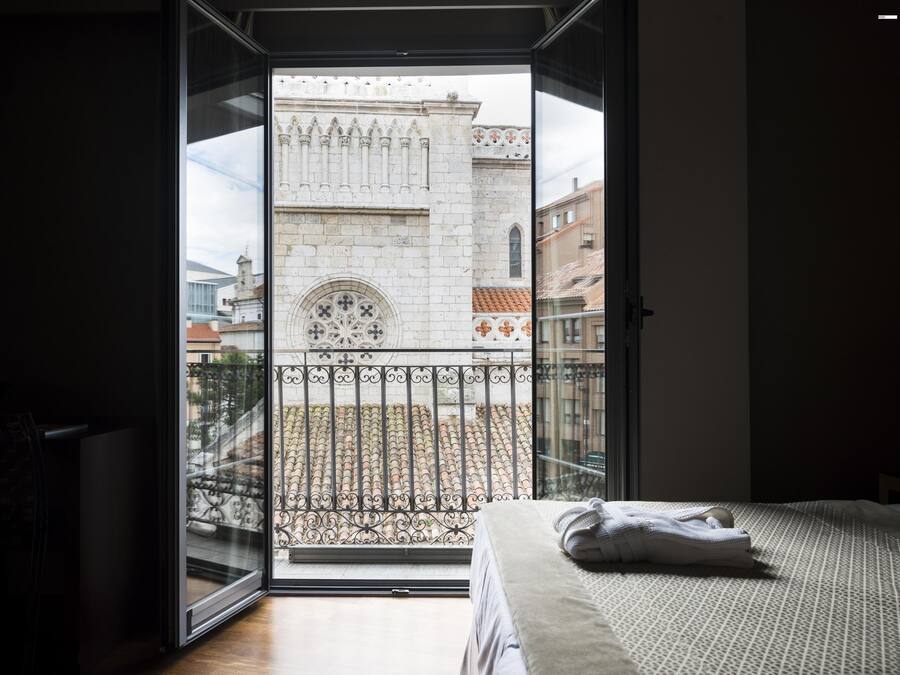 Un dormitorio con un amplio ventanal que da a un edificio histórico con un balcón ornamentado.