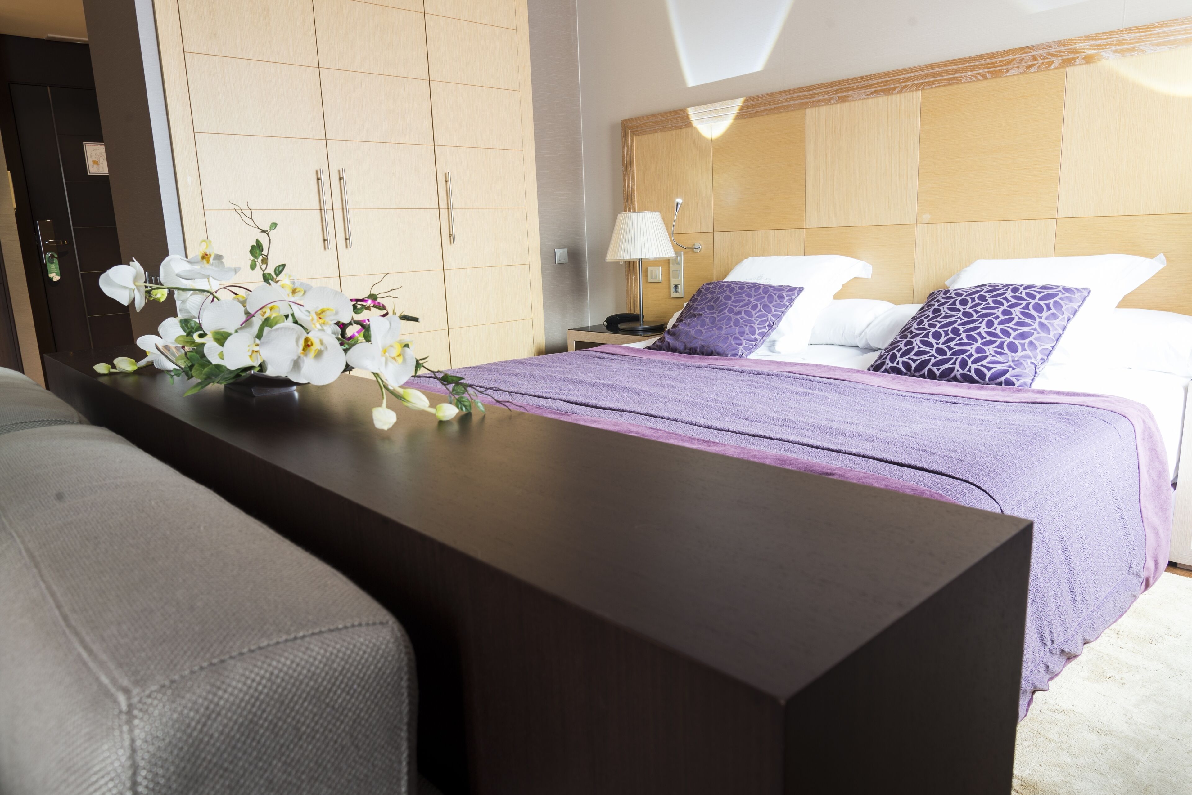 Een hotelkamer met een bed, een nachtkastje met een lamp en een bloemstuk.