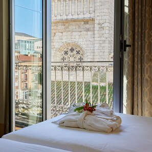 Ein Hotelzimmer mit Bett, Fenster mit Blick auf ein Gebäude mit einem dekorativen Fenster und einem Balkon mit Geländer.
