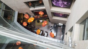 Un intérieur moderne avec une balustrade en verre incurvée, plusieurs niveaux et des suspensions lumineuses orange.