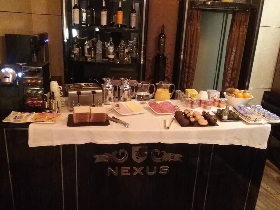 Una mesa de desayuno tipo bufé con diversos alimentos y bebidas, una máquina de café y un bar con botellas al fondo.