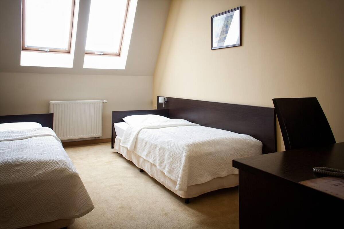 Ein Hotelzimmer mit zwei Einzelbetten, einem Schreibtisch und einem Stuhl. Es gibt Dachfenster und eine Heizung an der Wand.