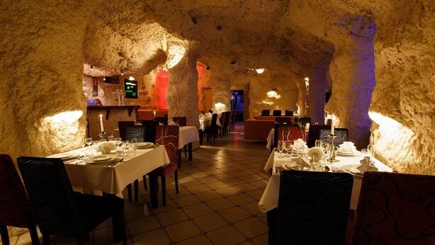 Un intérieur avec des tables dressées pour le repas, des murs en pierre et un sol carrelé.