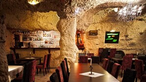 Un restaurant au décor rustique, avec des murs en pierre, une longue table en bois et des chaises à l’assise rembourrée de tissu rouge.