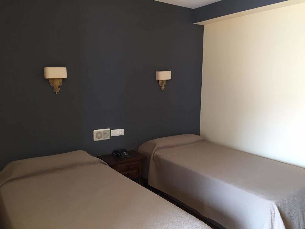 A hotel room with two single beds, a bedside table with a phone, and two wall-mounted lamps.