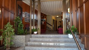 Una amplia escalera conduce a un segundo piso, flanqueada por paneles de madera y plantas en macetas.