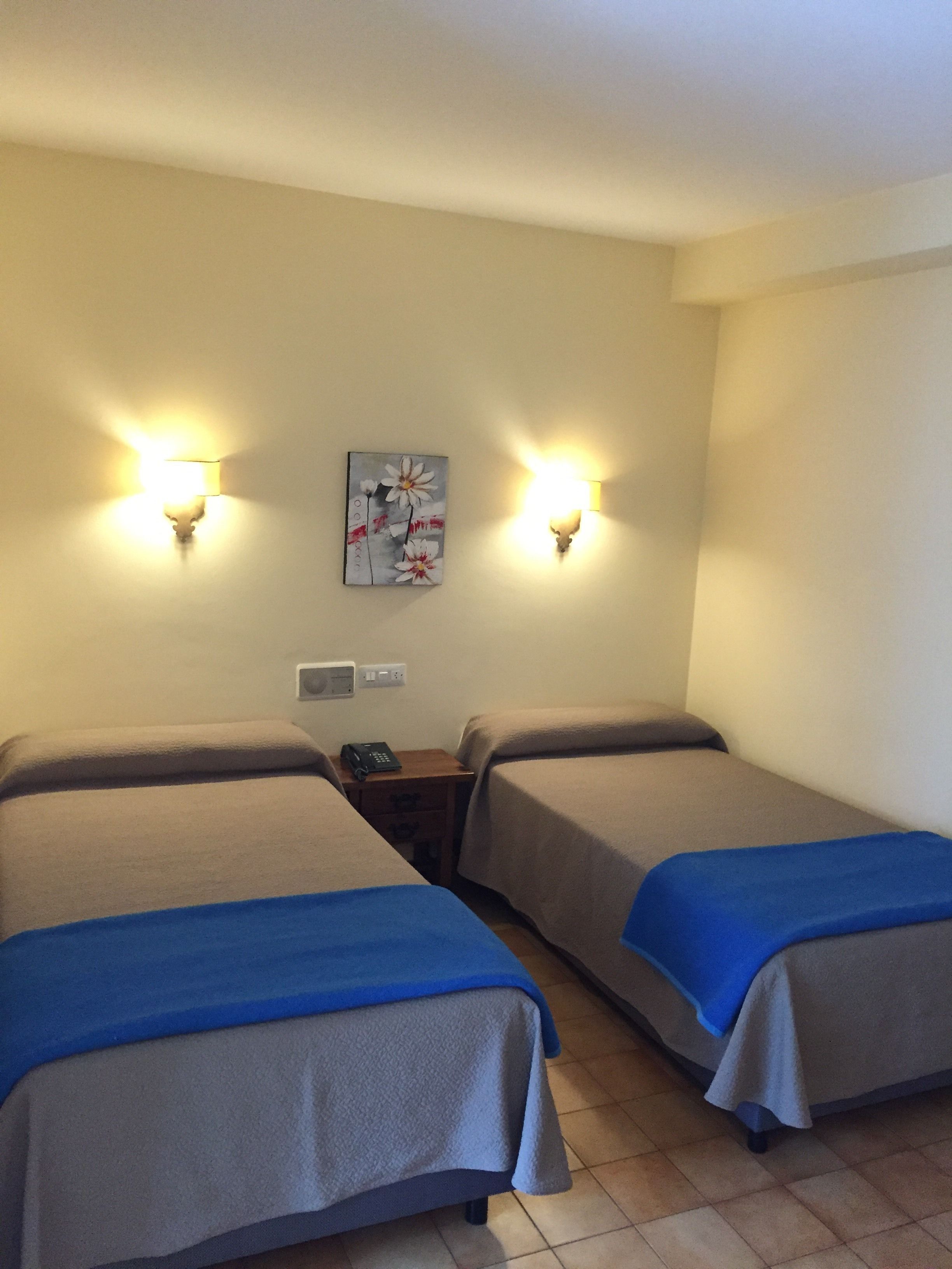 A hotel room with two beds, a nightstand with a phone, and wall-mounted lamps.