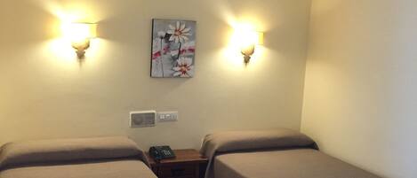 A hotel room with two beds, a nightstand with a phone, and wall-mounted lamps.