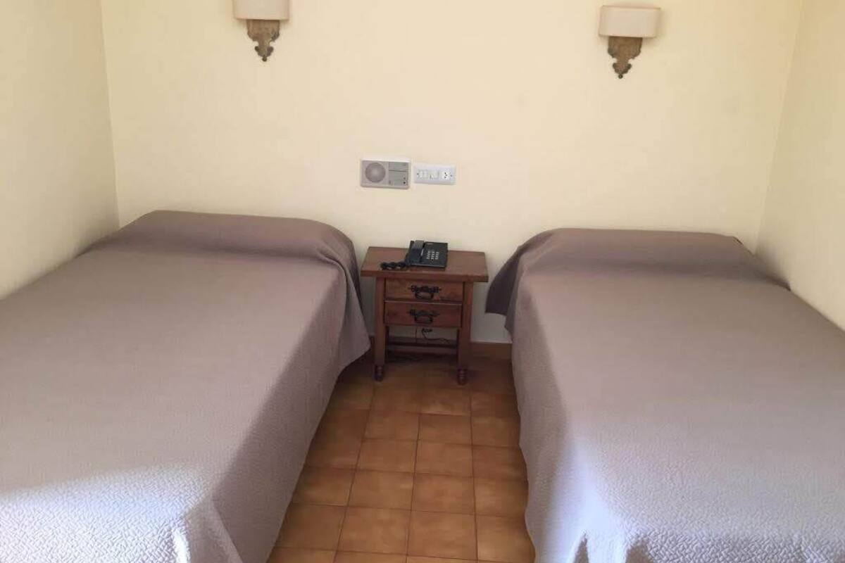 A room with two beds, a small table with a telephone, and wall-mounted lamps.