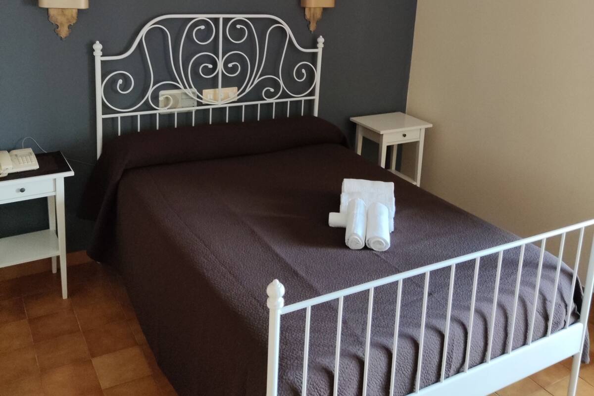A neatly made bed with a dark brown bedspread, two bedside tables with lamps, and a wall-mounted telephone.