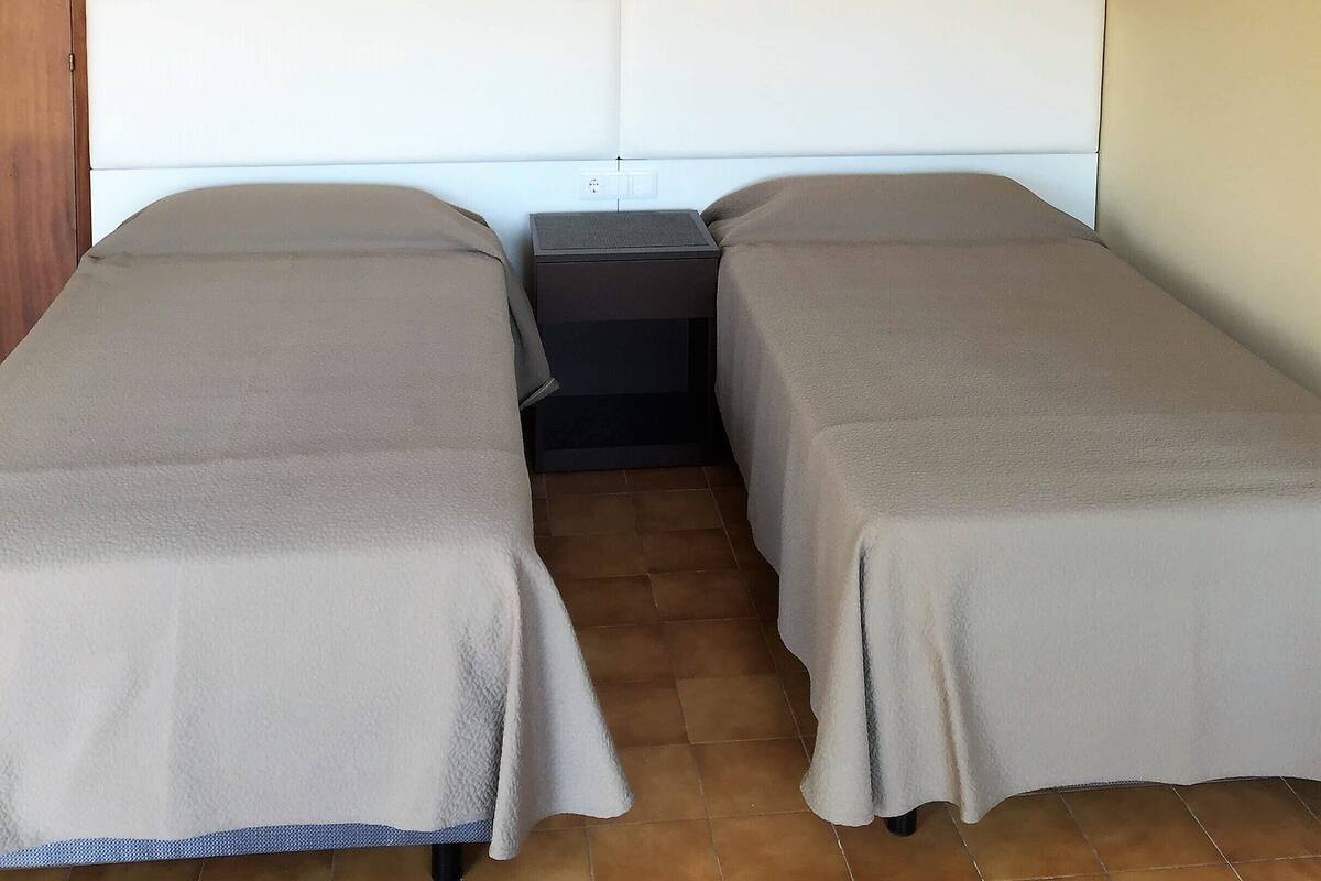 A room with two beds, a nightstand, and wall-mounted lamps.