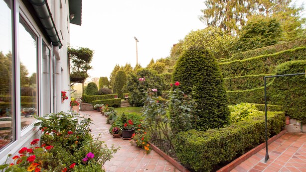 A well-maintained garden with various plants and flowers, a neatly trimmed hedge, and a tiled patio area. - Casa Rural Mailan (Aia)