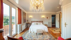 A spacious bedroom with a large bed, a chandelier, a view of the outdoors, and a balcony. - Casa Rural Mailan (Aia)