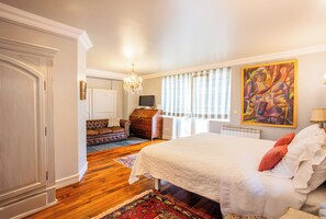 A bedroom with a large bed, a dresser, a television, and a painting on the wall.