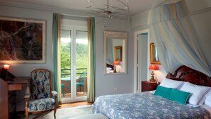 A bedroom with a large bed, a chair, a desk, and a balcony with a view of greenery. - Casa Rural Mailan (Aia)