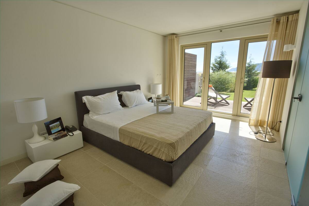 A modern bedroom with a large bed, bedside tables, and a view of the outdoors through a sliding glass door.