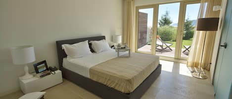 Un dormitorio moderno con una cama grande, mesitas de noche y vistas al exterior a través de una puerta corrediza de vidrio.