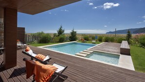 A modern outdoor pool area with two swimming pools, wooden deck, lounge chairs, and a view of the landscape. - Troia Residence Praia (Grandola)