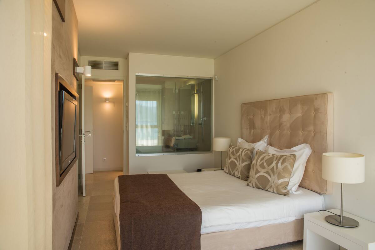 A hotel room with a bed, bedside lamps, a mirror, and a door.