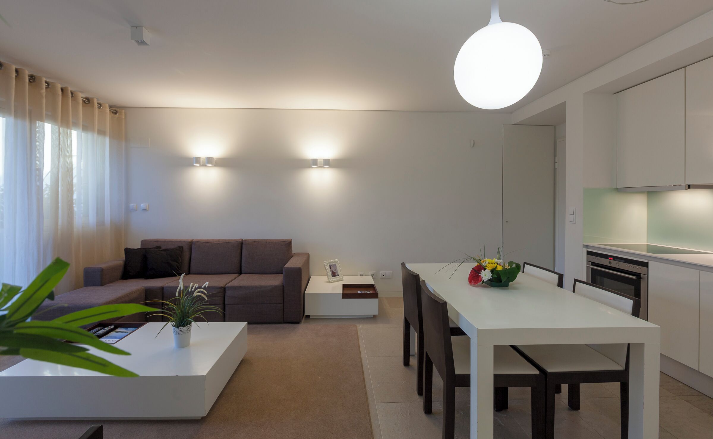 Una sala moderna con sofá, mesa de centro y mesa de comedor. Cuenta con una zona de cocina con estufa y armarios.
