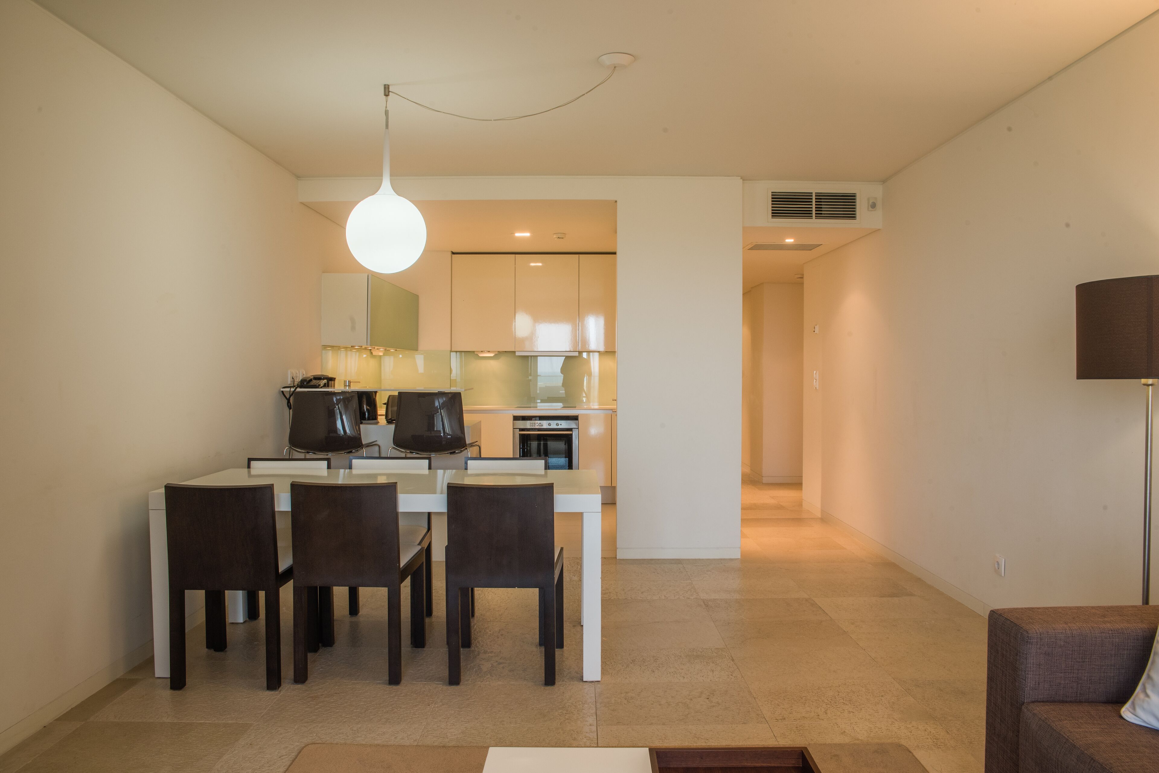 A modern kitchen with white cabinets, a dining table with four chairs, and a pendant light.