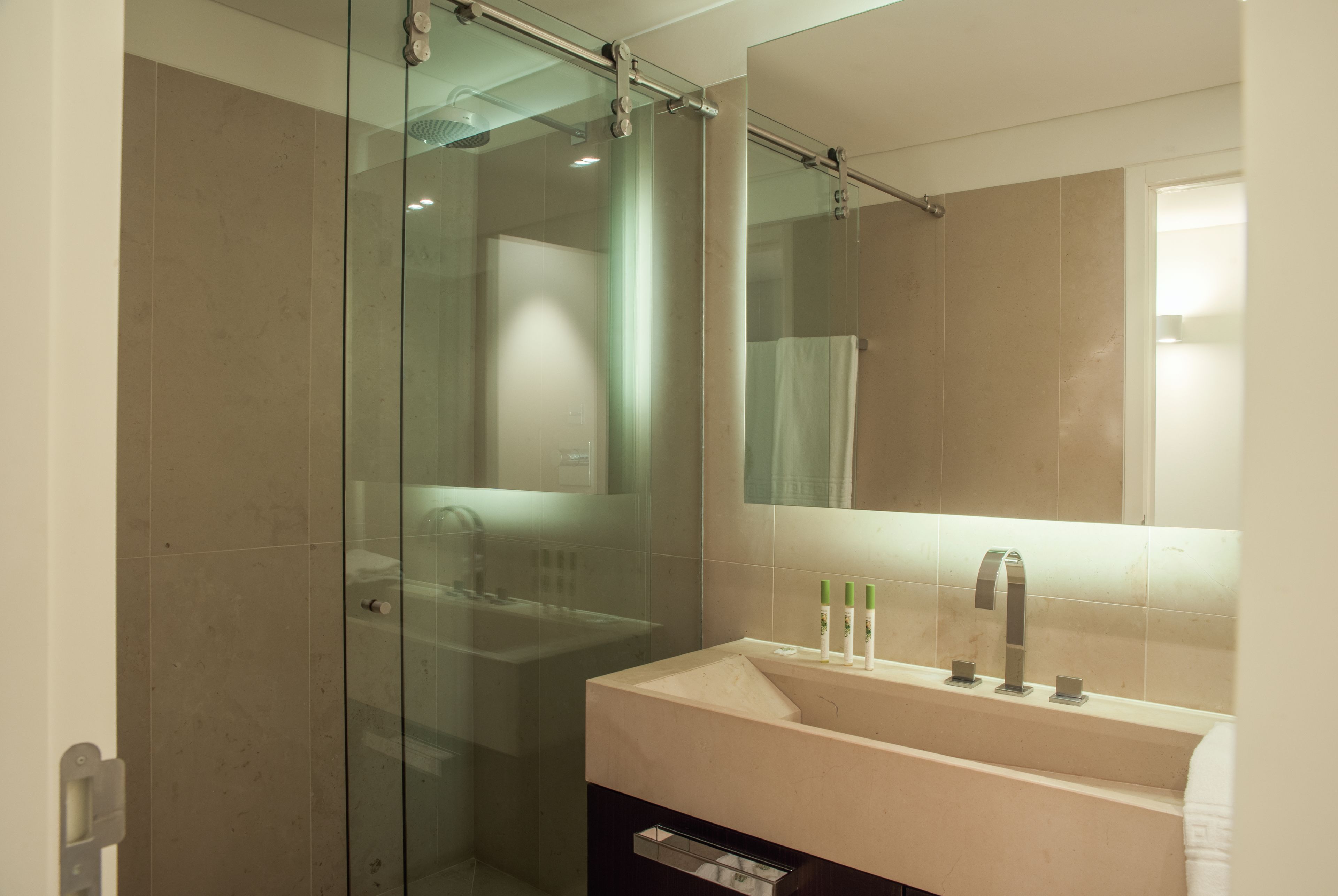 Ein modernes Badezimmer mit einer Duschkabine aus Glas, einem weißen Waschbecken mit Spiegel darüber und einem Handtuchhalter.