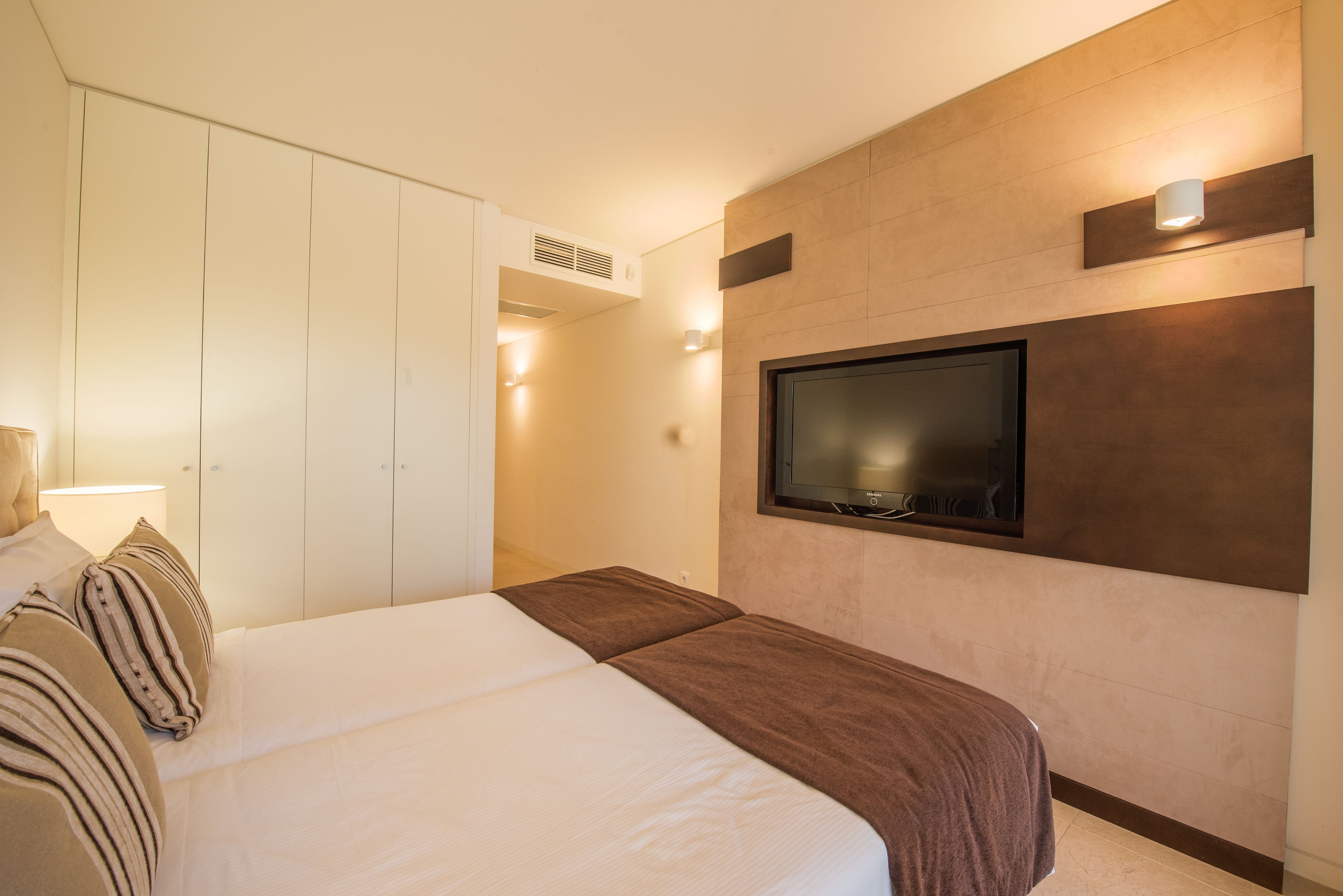 Een moderne hotelkamer met een groot bed, een aan de muur bevestigde televisie en een kledingkast.