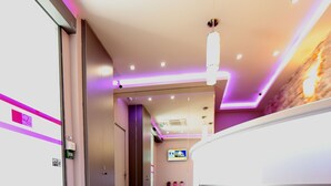 A modern reception area with a curved reception desk, a glass door entrance, and a hallway leading to elevators. - Sweet Hotel (Paris)