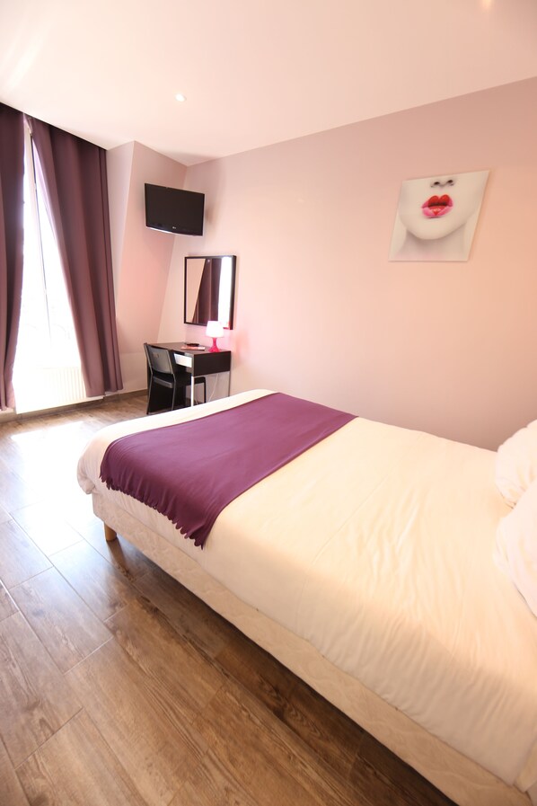 A hotel room with a bed, a desk, a chair, a TV, and a window with curtains.