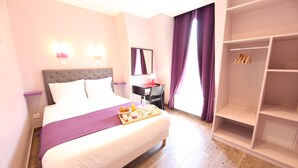A hotel room with a large bed, a bedside table with a lamp, a wardrobe, and a tray with breakfast items. - Sweet Hotel (Paris)