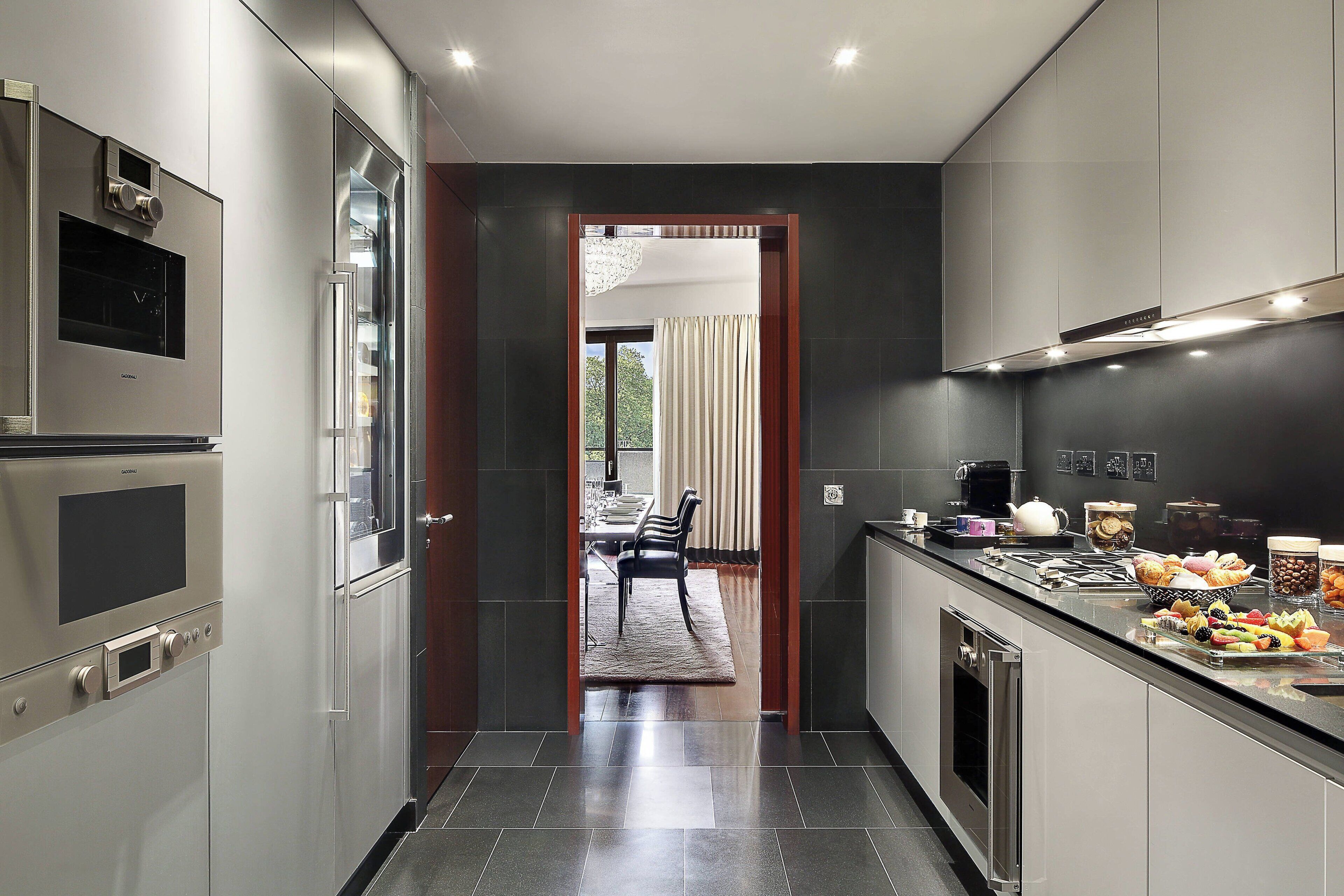A modern kitchen with stainless steel appliances, a dining area with a table and chairs, and a view through an open doorway to a dining room.