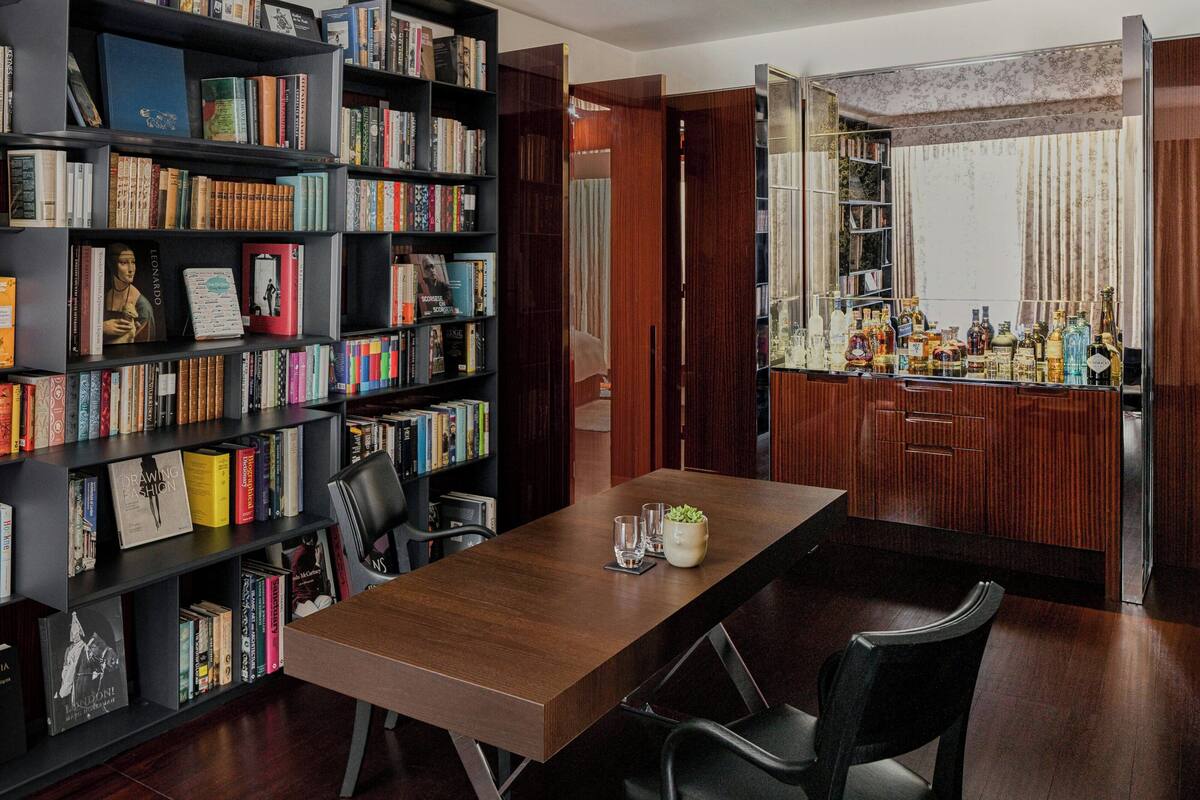 A room with a wooden table, black chairs, a bookshelf filled with books, and a bar area with bottles.