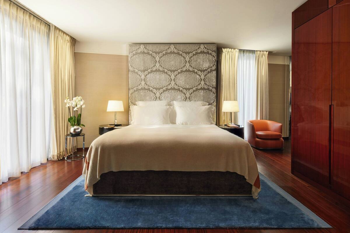 A hotel room with a large bed, two bedside tables, a nightstand, a chair, and a wardrobe.