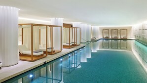 En swimmingpool med liggestole og solsenge, omgivet af hvide gardiner og en flisbeklædt væg.