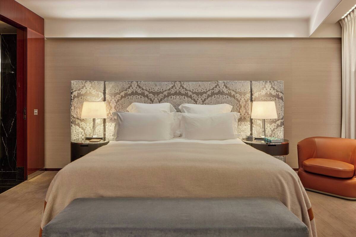 A hotel room with a large bed, two bedside lamps, a nightstand, and a leather armchair.