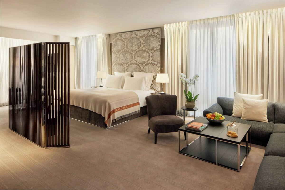 A hotel room with a bed, a sofa, a coffee table, and a decorative plant.