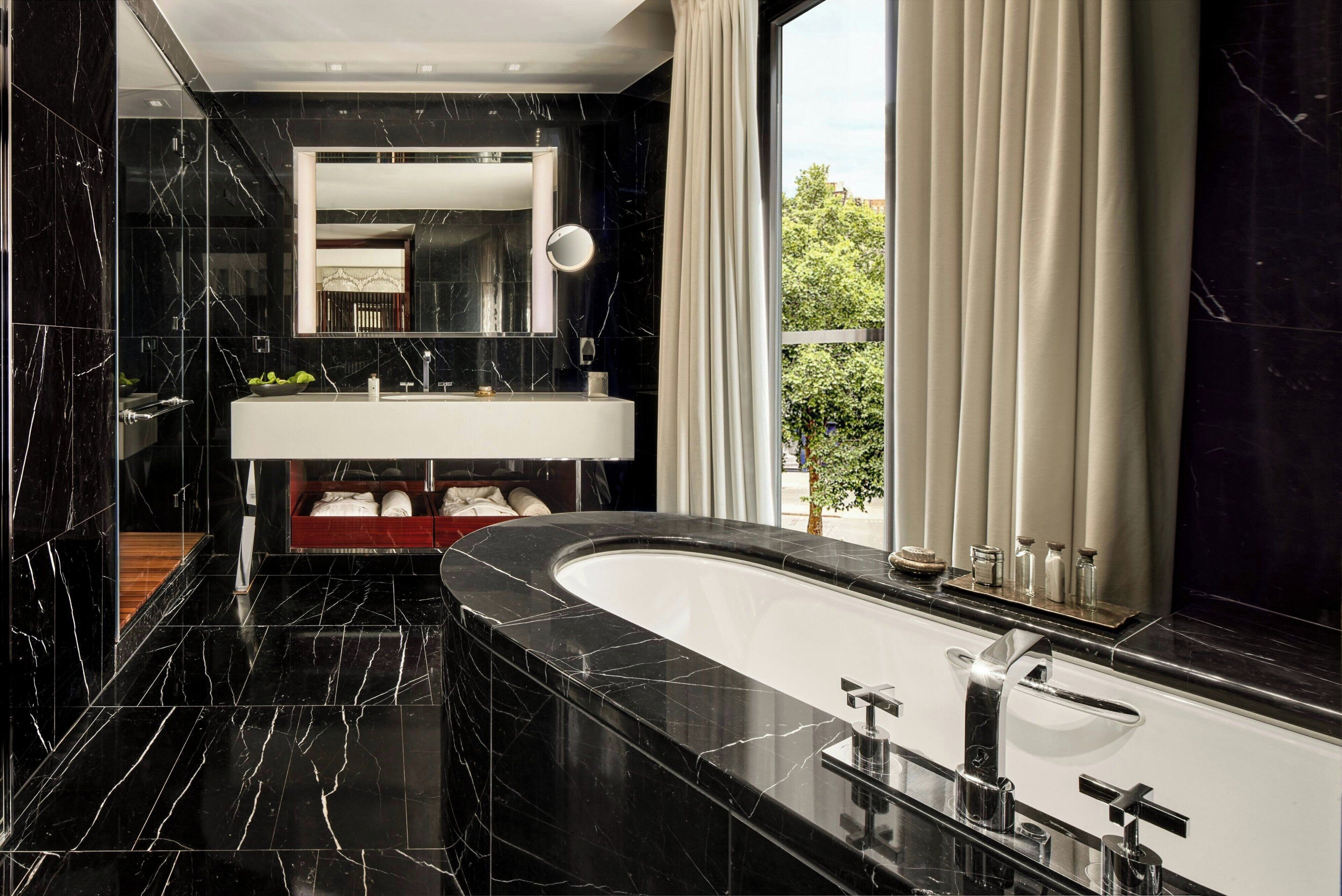 Une salle de bain moderne avec un grand lavabo en marbre noir, une baignoire sur pieds et un grand miroir au-dessus du lavabo.