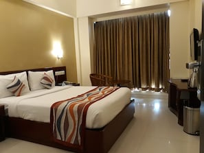 A hotel room with a large bed, a desk, a chair, a TV, and a trash bin.