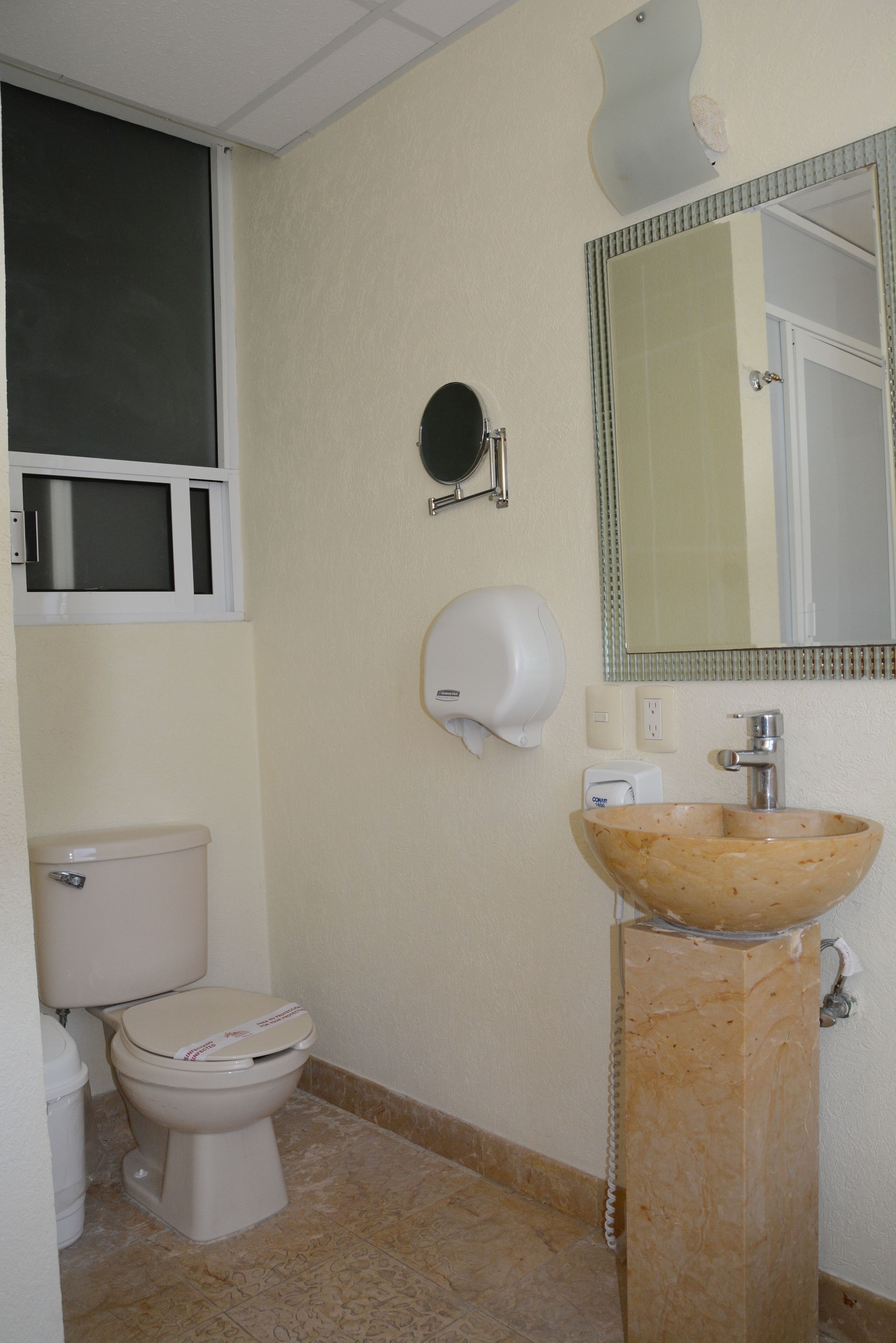A bathroom with a toilet, a sink with a marble basin, a mirror, and a soap dispenser.
