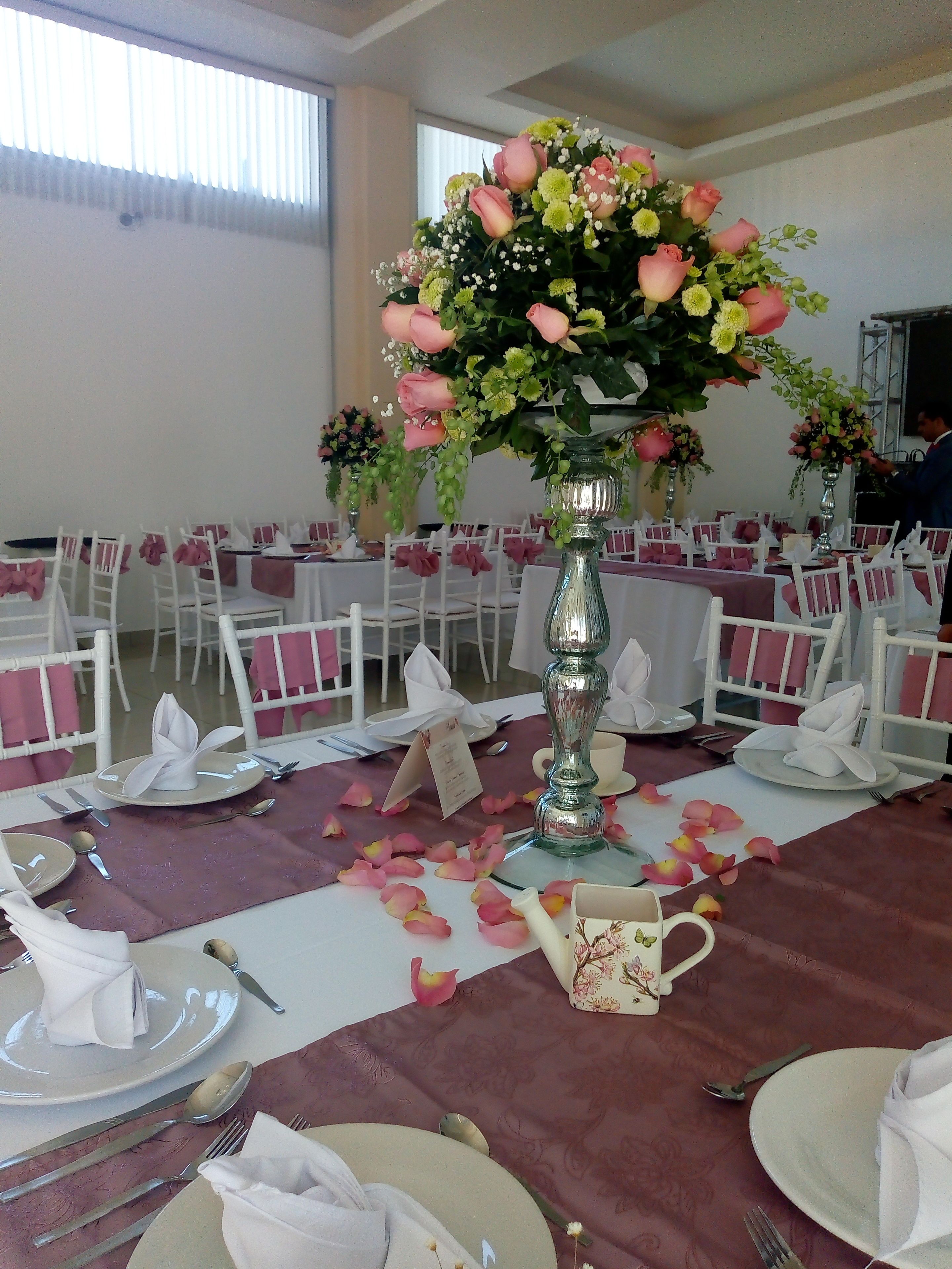 Un salón de banquetes con mesas redondas dispuestas para un evento formal, con sillas blancas, manteles y centros de mesa florales.