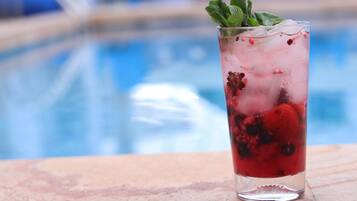 A tall glass with ice and berries, placed on a stone surface near a pool.